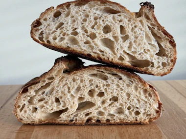 Two halves of an open-crumb sourdough loaf on a wooden board.