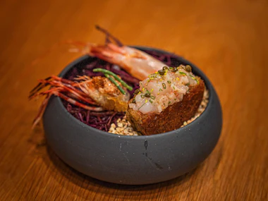 Shrimp with shredded red cabbage and a topped crouton in a dark bowl.