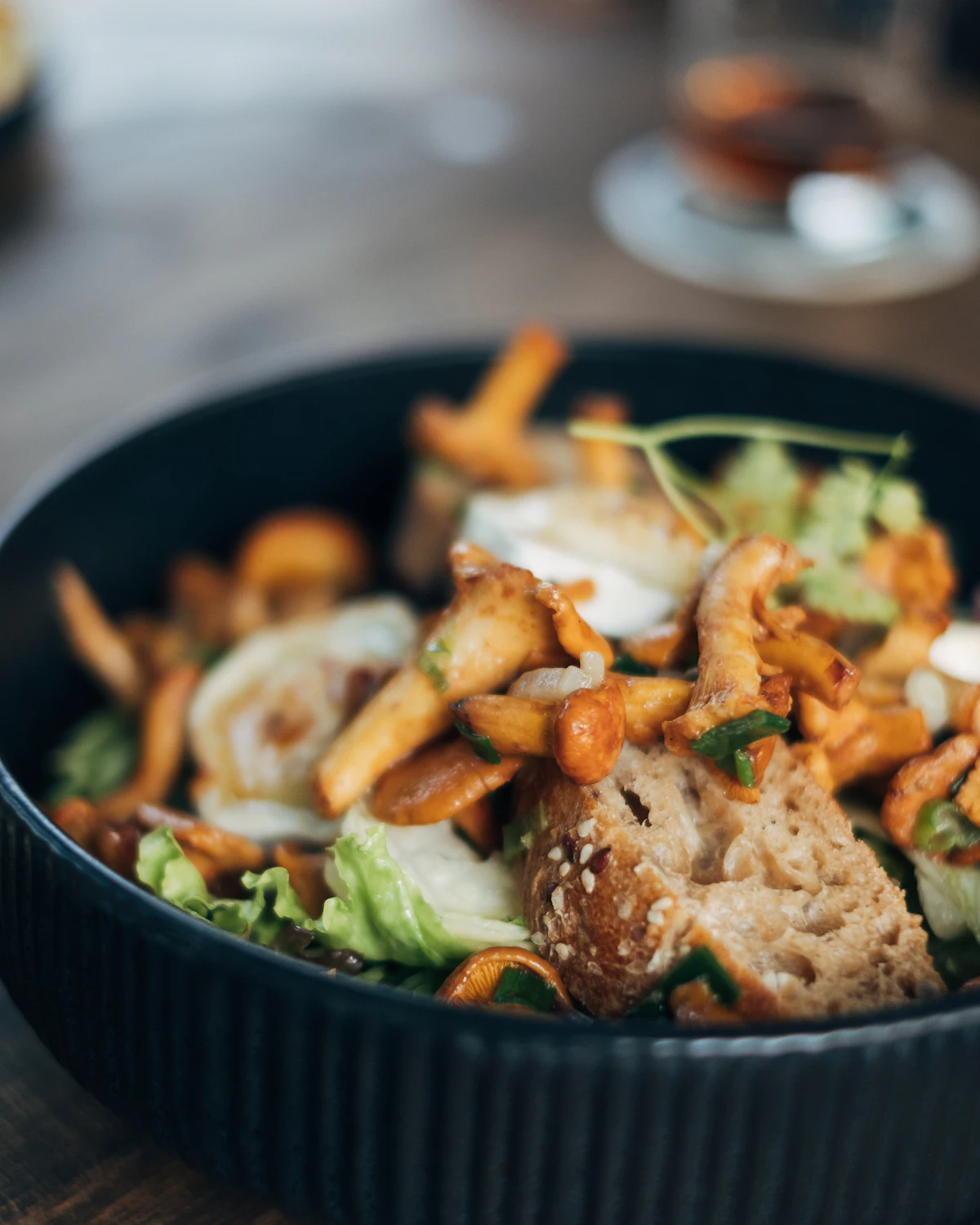 Chanterelles, charred leeks and torn bread piled off-centre in a dark ridged stoneware bowl.