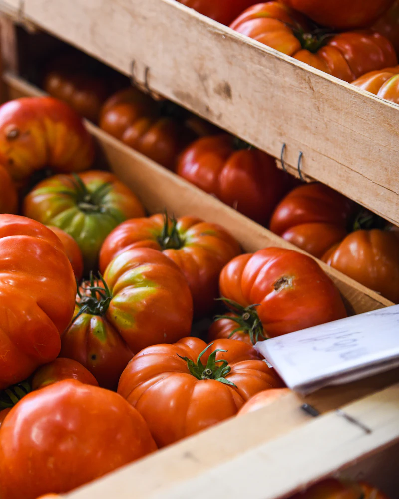 Heirloom tomatoes stacked in wooden crates at a covered market stall.