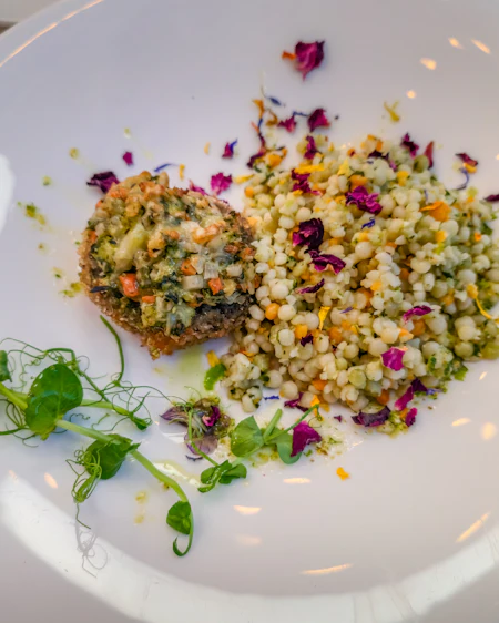Courgette fritter beside pearl couscous, pea shoots and scattered flower petals.