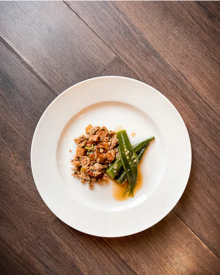 Slow lamb shoulder with okra and green harissa spooned low across a white plate.