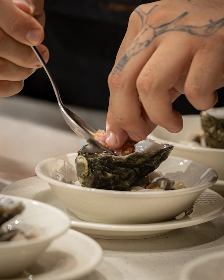 A hand finishing an oyster with a small spoon under low directional light.