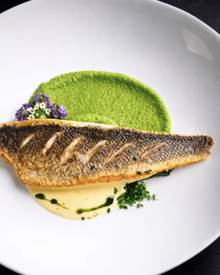 Crisp-skinned sea bass over pea cream with charred lemon and pea shoots.