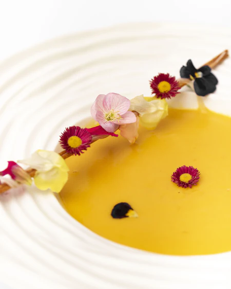 Amber squash velouté in a ridged white bowl, scattered with marigold petals.