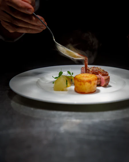 A spoon pouring dark red wine glaze over sliced dry-aged sirloin.
