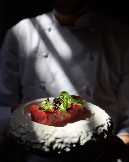 Hands presenting sliced raw tuna loin on a mottled black and white ceramic plate.